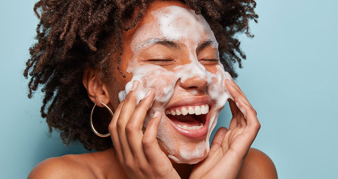Mulher negra sorri ao fazer sua limpeza facial